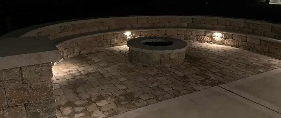 A paver patio and custom fire pit at night with landscape lighting in Columbia, IL.